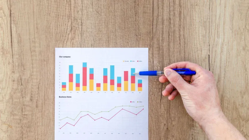 A hand holding a pen over a printed sheet of monthly business charts